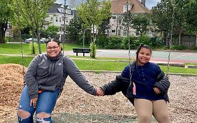 big and little sister holding hands on a swing in a park.