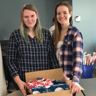 two young women holding a box filled with wrapped presents